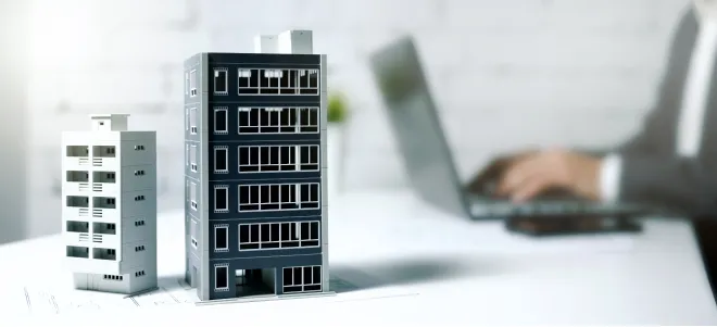 Geschäftsmann arbeitet am Laptop im Büro mit Gebäudemodellen auf dem Tisch